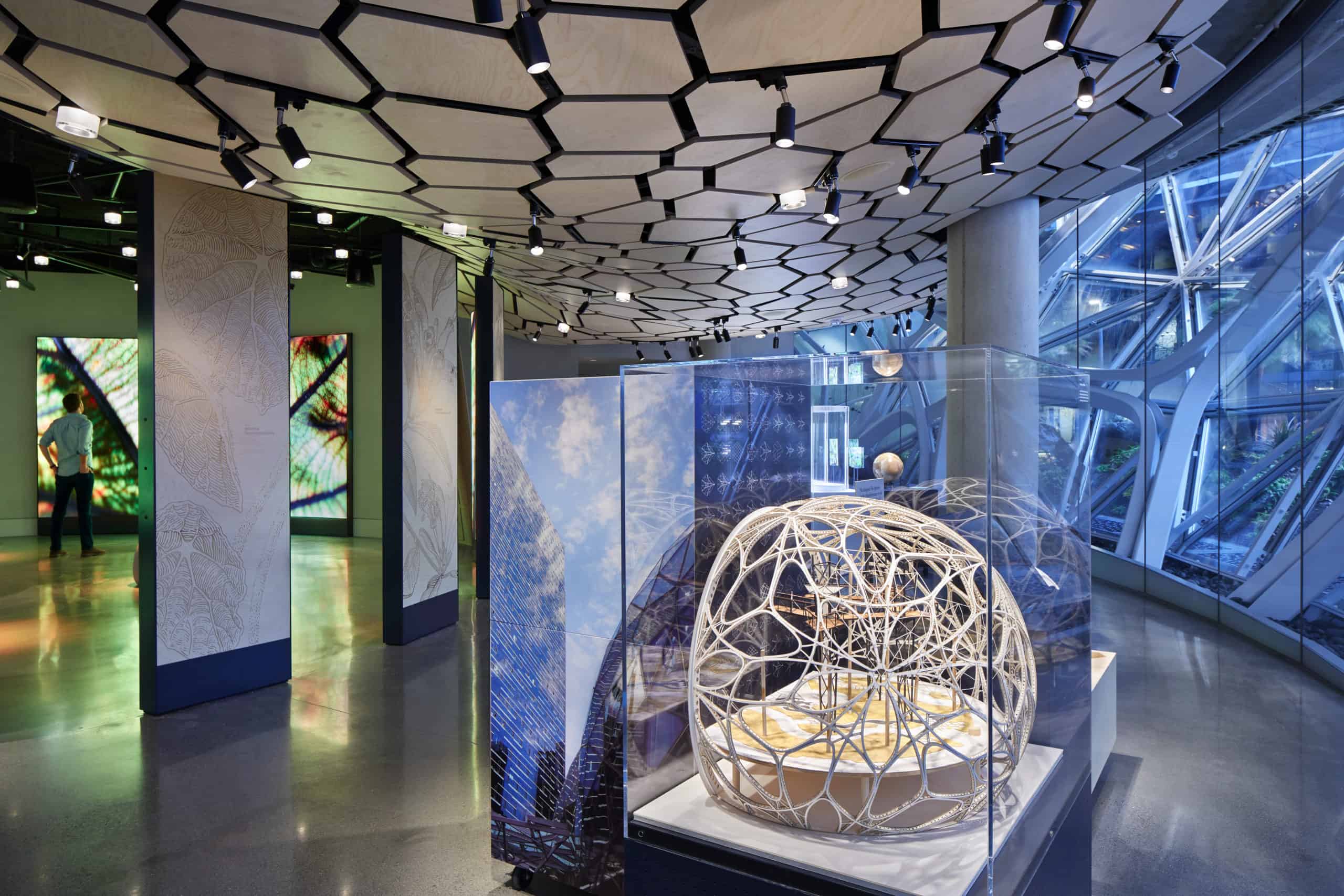 Modern exhibit with geometric ceiling patterns, a spherical model, colorful murals, large windows; person in the background.