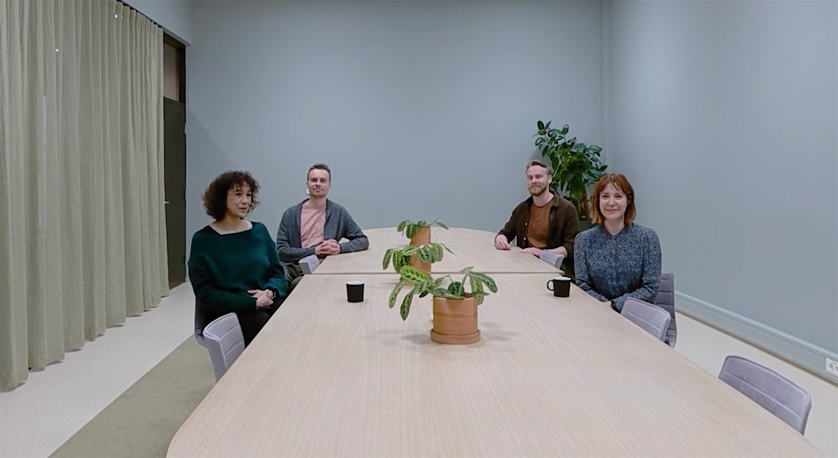 Meeting room with four people sat at the table. There are two men and two women.