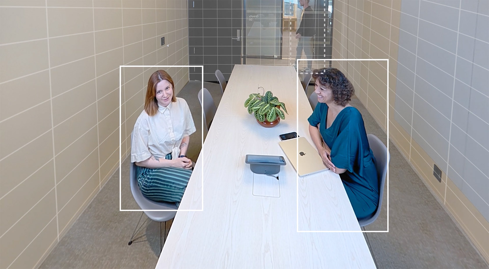 Two women sat in a meeting room with the camera's tracking function highlighting the two.