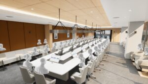 Sala de reuniones extragrande con una mesa alargada. Los asistentes disponen de monitores y micrófonos individuales. La mesa está orientada hacia una gran pantalla montada en la pared situada al fondo de la sala.